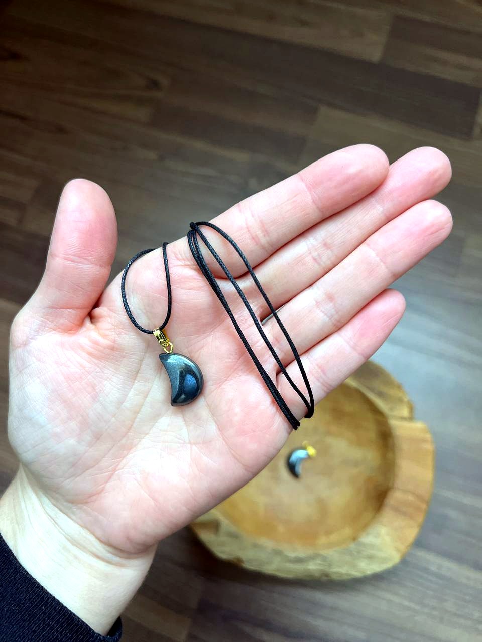 Hämatit Mond Anhänger mit schwarzem Baumwollband auf der Hand