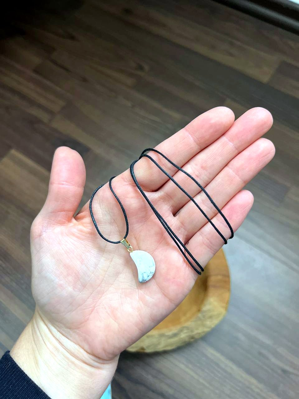 Magnesit Mond Anhänger mit schwarzem Baumwollband auf der Hand