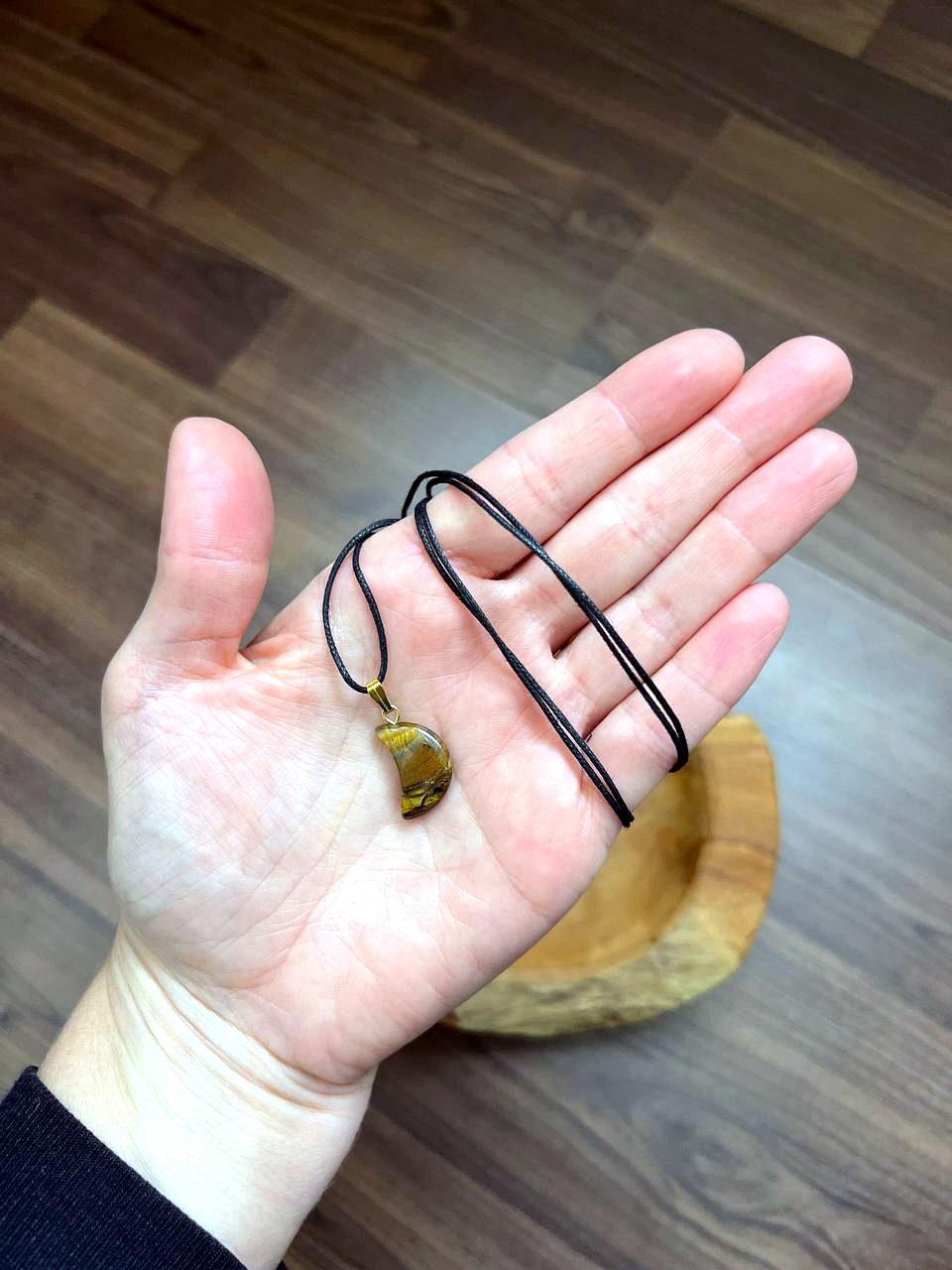 Tigerauge Mond Anhänger mit schwarzem Baumwollband auf der Hand