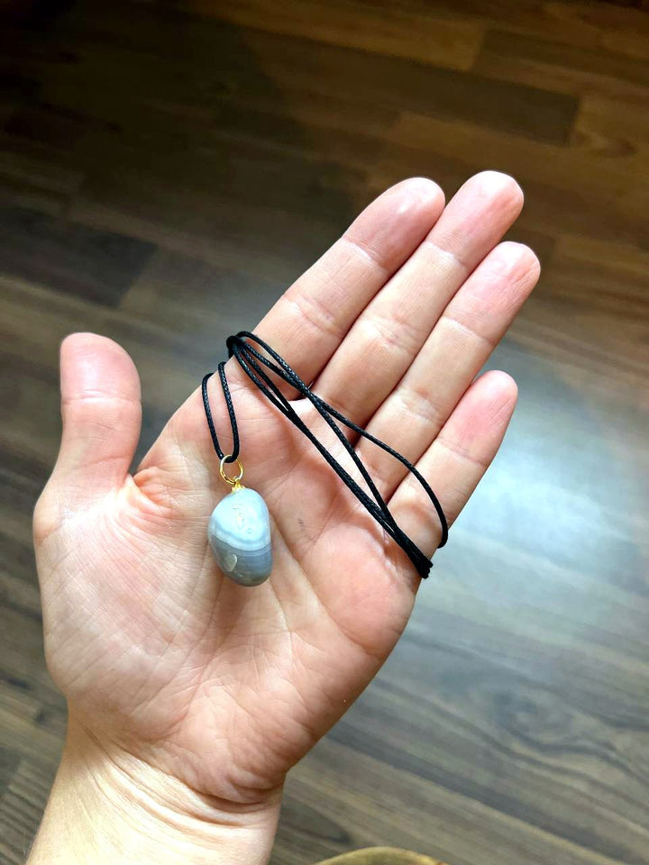 Achat Trommelstein Anhänger mit schwarzem Baumwollband auf der Hand