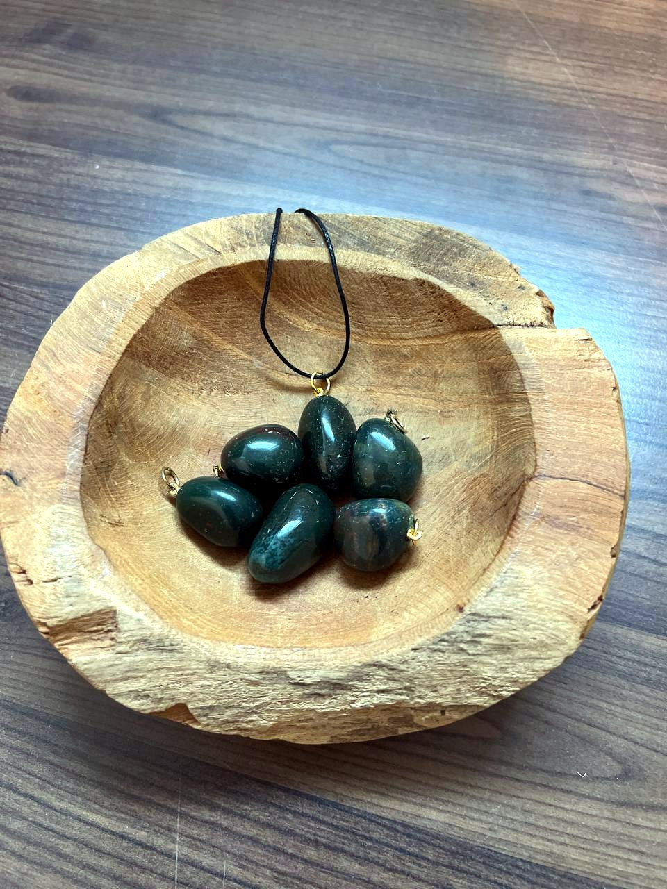 Heliotrop Trommelstein Anhänger mit goldener Öse in einer Holzschale