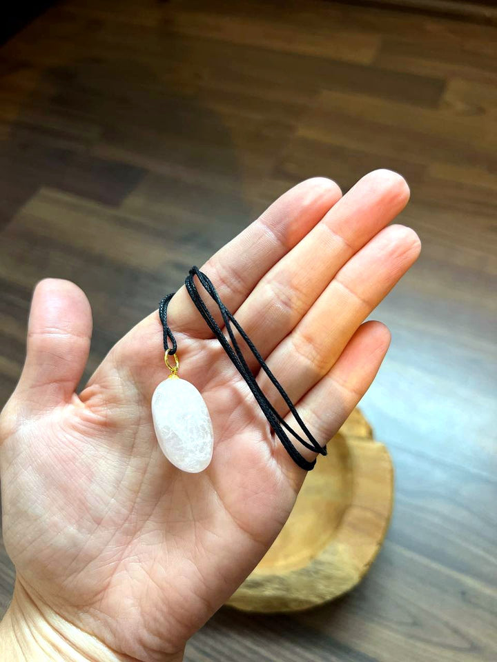 Rosenquarz Trommelstein Anhänger mit schwarzem Baumwollband auf der Hand