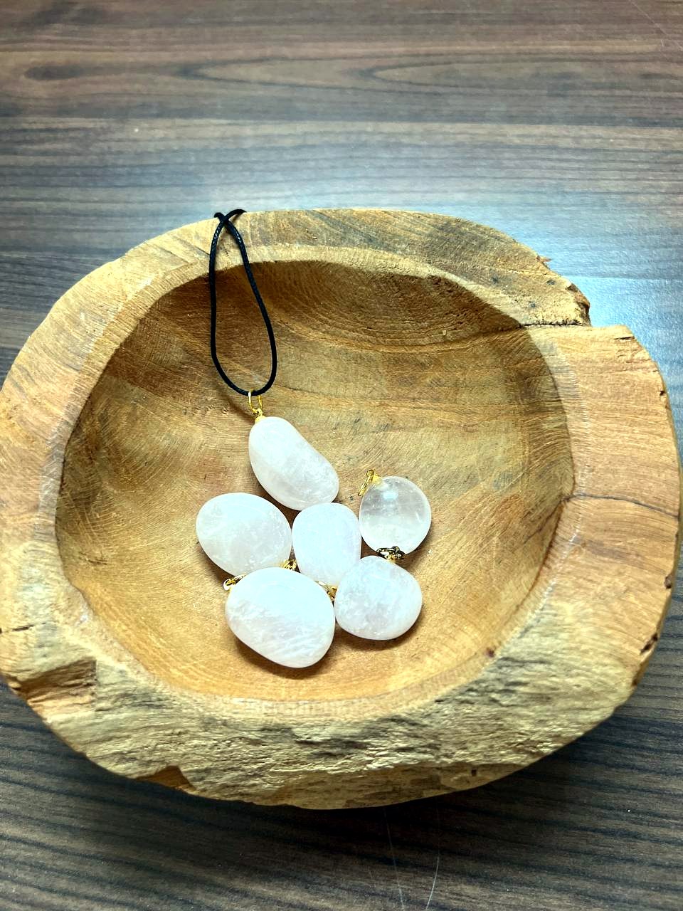 Rosenquarz Trommelstein Anhänger mit goldener Öse in einer Holzschale